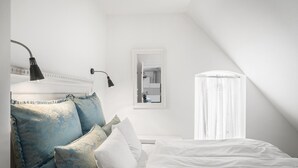 Une chambre à coucher avec un lit, une lampe de chevet, une fenêtre avec des rideaux et un miroir au mur.
