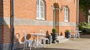 Un bâtiment en briques avec des fenêtres à cadre blanc et un espace extérieur aménagé avec des chaises et des tables en métal.