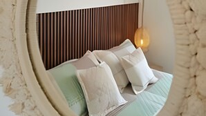 A circular mirror with a textured frame, reflecting a bed with pillows and a hanging light fixture. - San Gil Plaza suite 502 (San Gil)