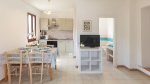 Een moderne keuken met een eethoek, een televisie op een standaard, en een badkamer zichtbaar door een geopende deur.