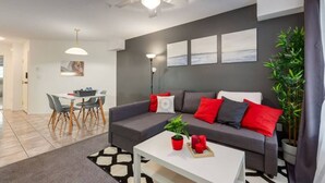 A modern living room with a grey sofa, red and white cushions, a white coffee table, and a dining area with a table and chairs. - Modern Dream @ Fairmont (accessible entrance) (Fairmont Hot Springs)