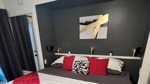 A hotel room with a bed, a red throw blanket, a white and red pillow, a black and white pillow, and a gold abstract painting on the wall. - Modern Dream @ Fairmont (accessible entrance) (Fairmont Hot Springs)