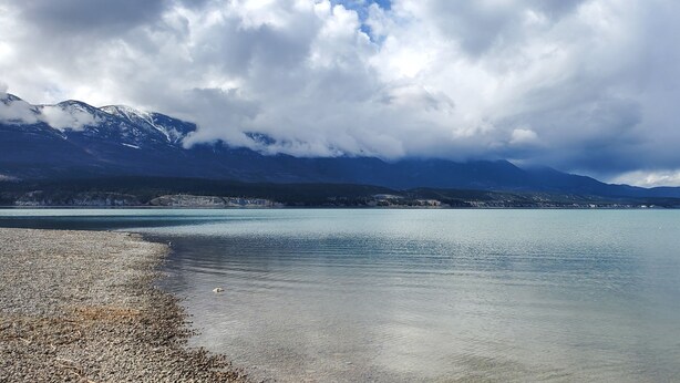 A calm lake with mountains in the background and a pebble beach in the foreground. - Modern Dream @ Fairmont (accessible entrance) (Fairmont Hot Springs)