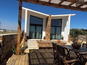 Ein modernes Haus mit großen Glaswänden, einer Holzterrasse und einer Steinpfeiler.