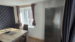 Une cuisine moderne avec une table à manger en bois, un mur noir texturé intégré, un réfrigérateur en acier inoxydable et une fenêtre avec des rideaux.