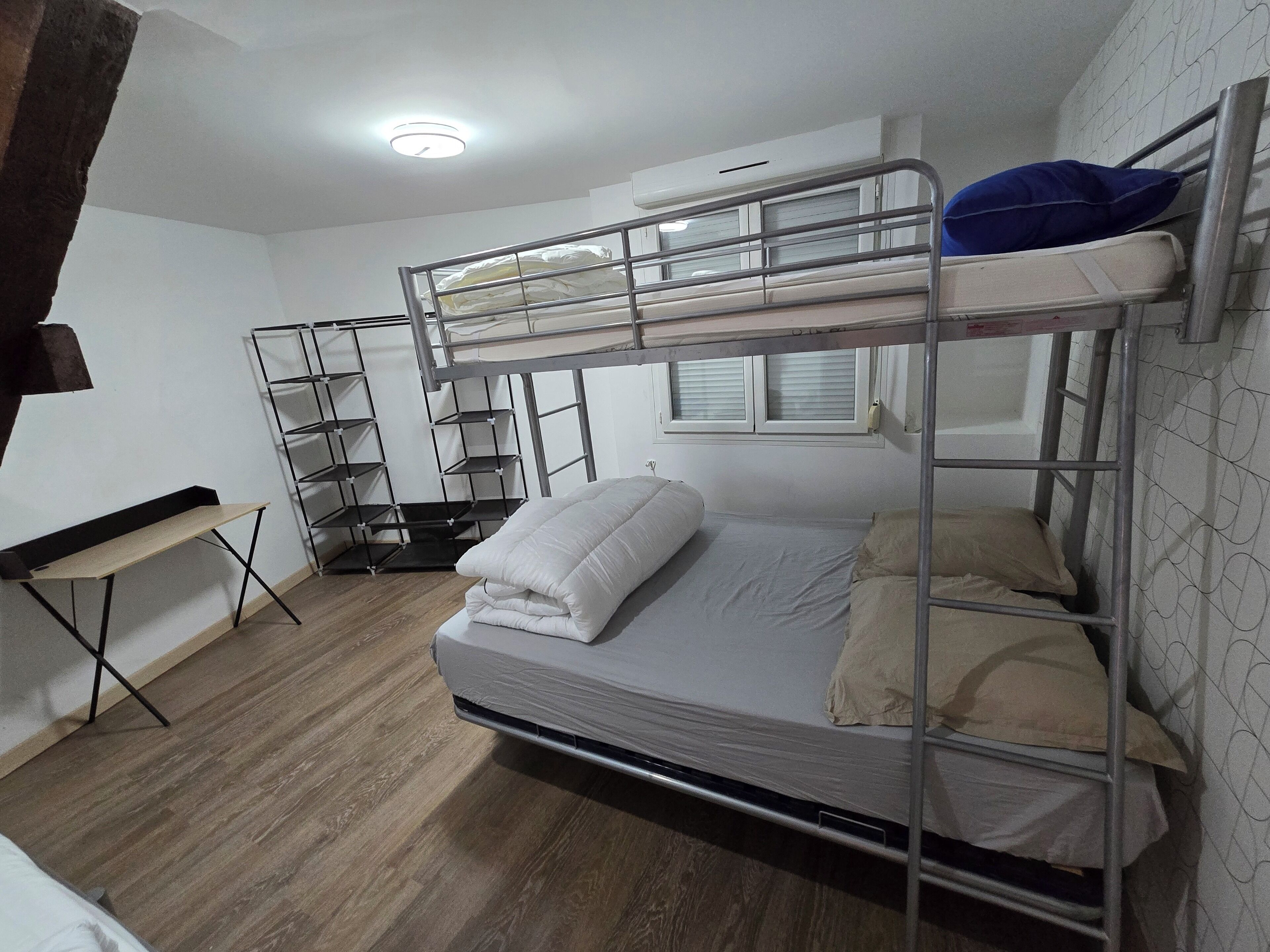 Een slaapkamer met stapelbed, bureau en planken.
