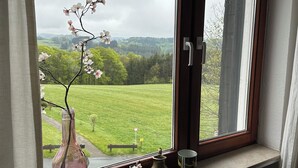 Une fenêtre donnant sur un champ verdoyant et des arbres, un vase rempli de fleurs et un radiateur en dessous.