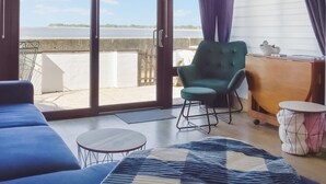 Une pièce avec vue sur la mer, un fauteuil vert, une petite table ronde et un tapis bleu à motifs.