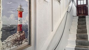 Un escalier muni d’une rampe, un tableau encadré représentant un phare et une pancarte indiquant « VERS LE BEAU ».