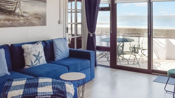 Un canapé bleu orné d’oreillers en forme d’étoiles de mer, une petite table ronde et une vue sur l’océan par une porte vitrée.