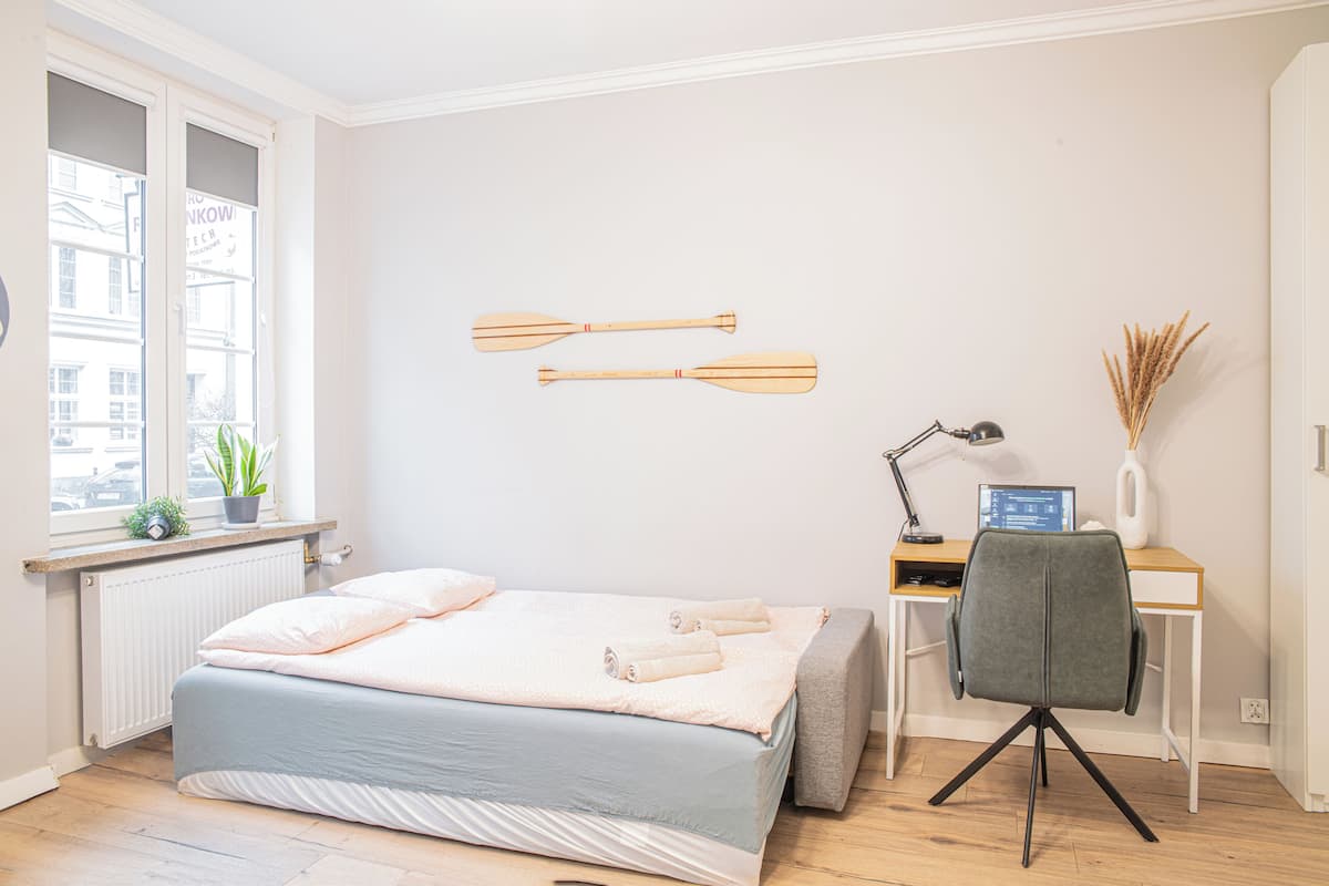 A bedroom with a bed, a desk, a chair, a window, and a radiator.