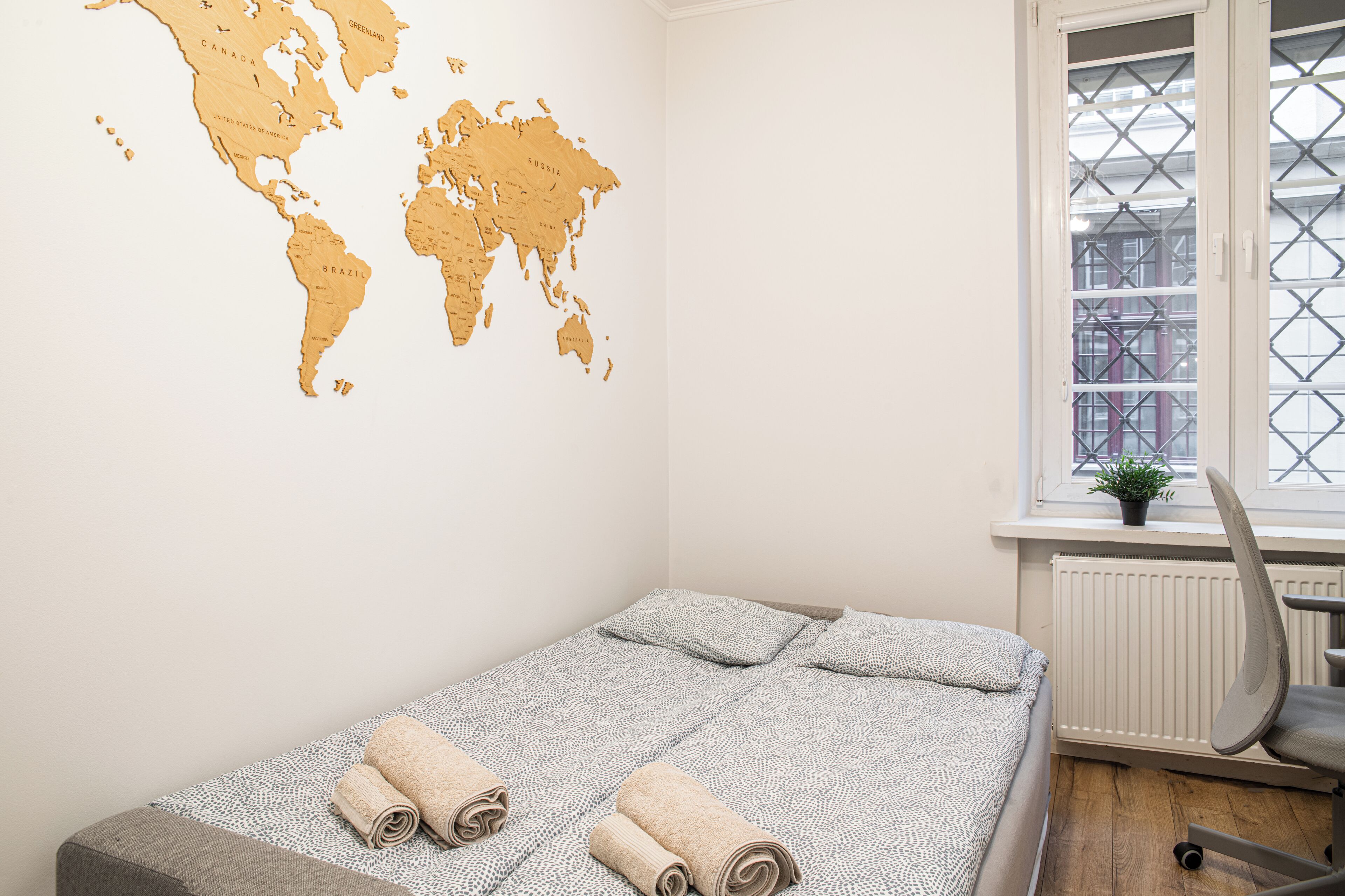 A room with a bed, a world map on the wall, a window with a view of buildings, and a radiator.