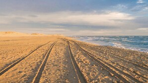 Una playa arenosa con surcos de neumáticos que conducen al agua.