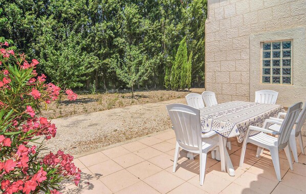 Un patio al aire libre con una mesa y sillas, rodeado por un muro de piedra y una arboleda densa.