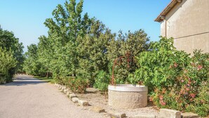 Un camino de grava que conduce a un edificio con una jardinera de piedra y una pérgola de metal con flores.