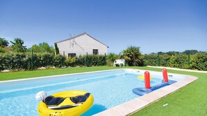 Una piscina con flotadores, una silla blanca, césped cuidado y un edificio al fondo.