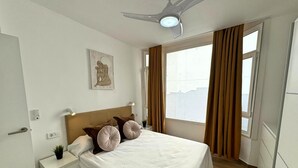 Une chambre d’hôtel bien rangée, avec un lit, des tables de chevet, un ventilateur de plafond et une fenêtre avec des rideaux.