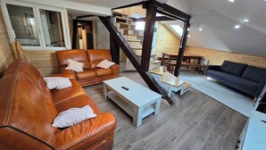 Ein Loft-Wohnzimmer mit Treppe, Ledersofas, Holztischen und Blick zum Himmel.