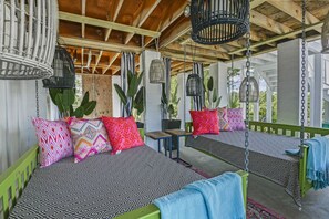 A covered outdoor seating area with two swing beds, hanging birdcages, and potted plants. - Waterfront Bliss in Bay St. Louis| Sleeps 4 | Private Pool | Bay Views! (Bay St. Louis)