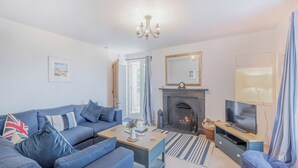 A living room with a sofa, coffee table, fireplace, television, and a window with curtains. - Discover coastal tranquility in Millhouse Cottage on Budle Bay. (Bamburgh)