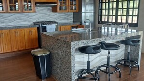 A modern kitchen with wooden cabinets, a granite countertop, a stainless steel refrigerator, and a large window.