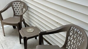 Un patio con dos sillas y una mesita, frente a una pared exterior blanca.