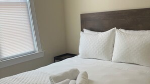 Una cama bien hecha con una colcha blanca acolchada y falda con volantes, un cabecero de madera y almohadas blancas.