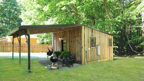 A wooden cabin with a covered patio, a grill, and a chair.
