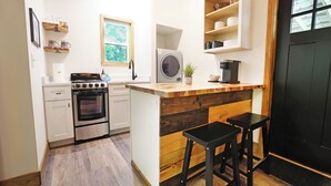 A compact kitchen with a built-in oven, a coffee machine, and wooden bar stools.