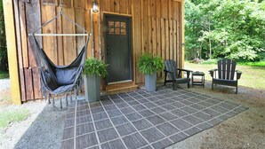 A wooden cabin with a hammock, two Adirondack chairs, and a door with a window.