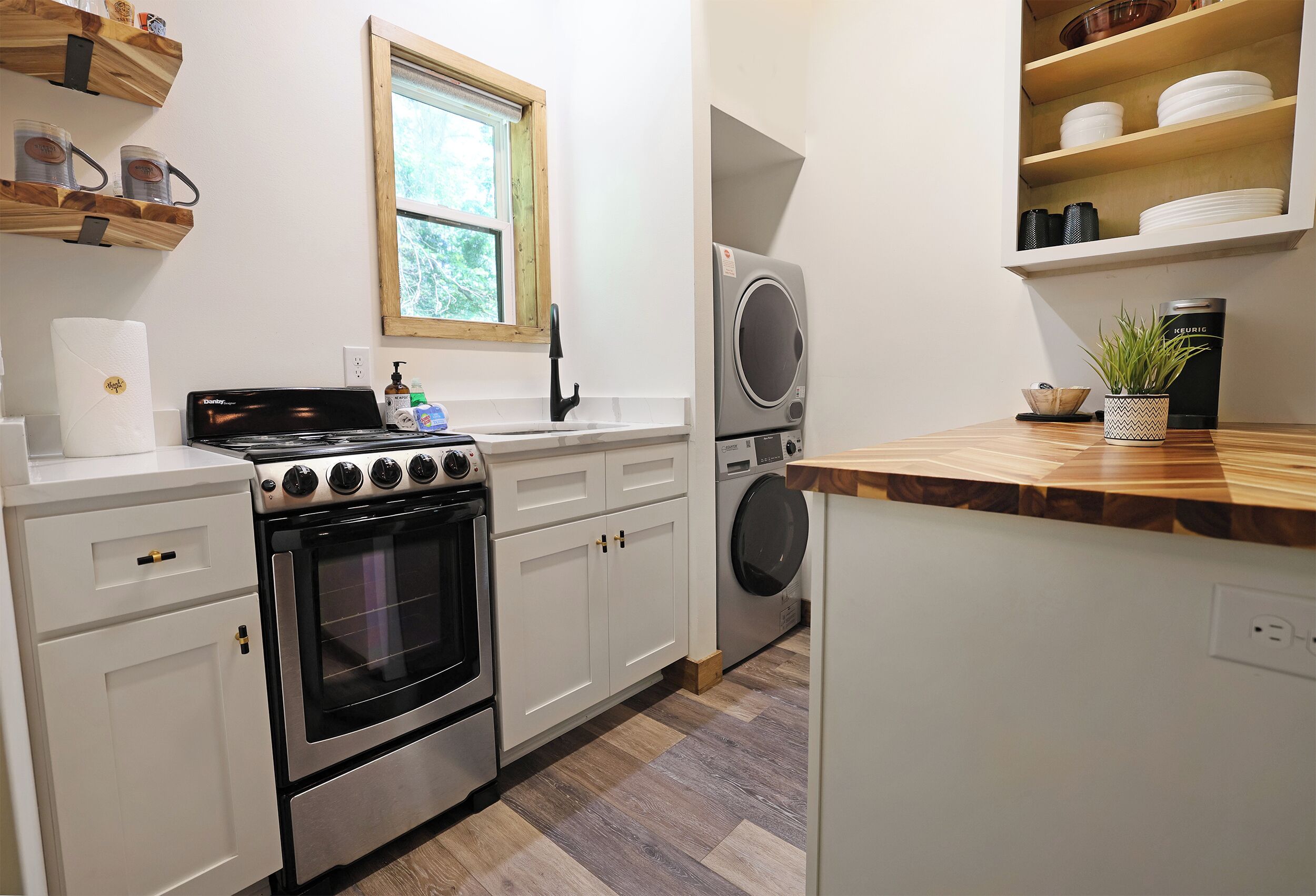 Una cocina con armarios blancos, estufa, lavadora y ventana.