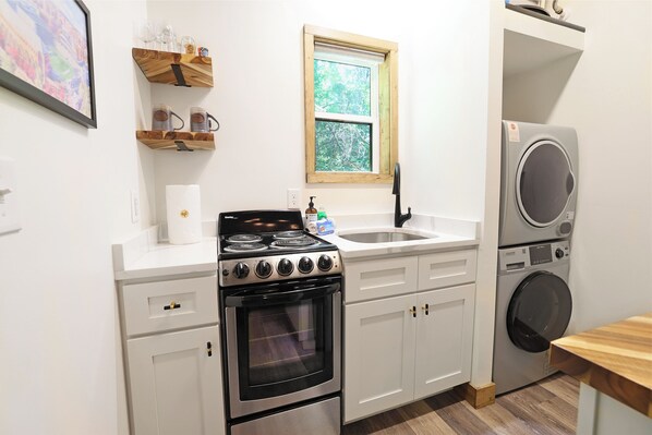 Una cocina con armarios blancos, estufa, lavabo y lavadora.