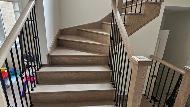 Eine Holztreppe mit schwarzen Geländern, die zu einer oberen Etage führt.