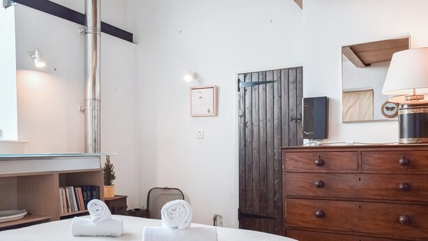 Ein ordentlich eingerichtetes Schlafzimmer mit einem Bett, einer Holzkommode, einem Spiegel und einem an der Wand montierten Fernseher.