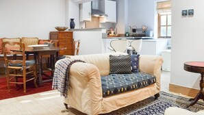 Ein Wohnzimmer mit einer Couch, einem Esstisch, Stühlen und einer Küchenzeile im Hintergrund.