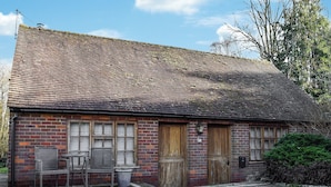 Ein Backsteinhaus mit Ziegeldach, zwei Holztüren und einer kleinen Veranda mit Stuhl und Mülleimer.
