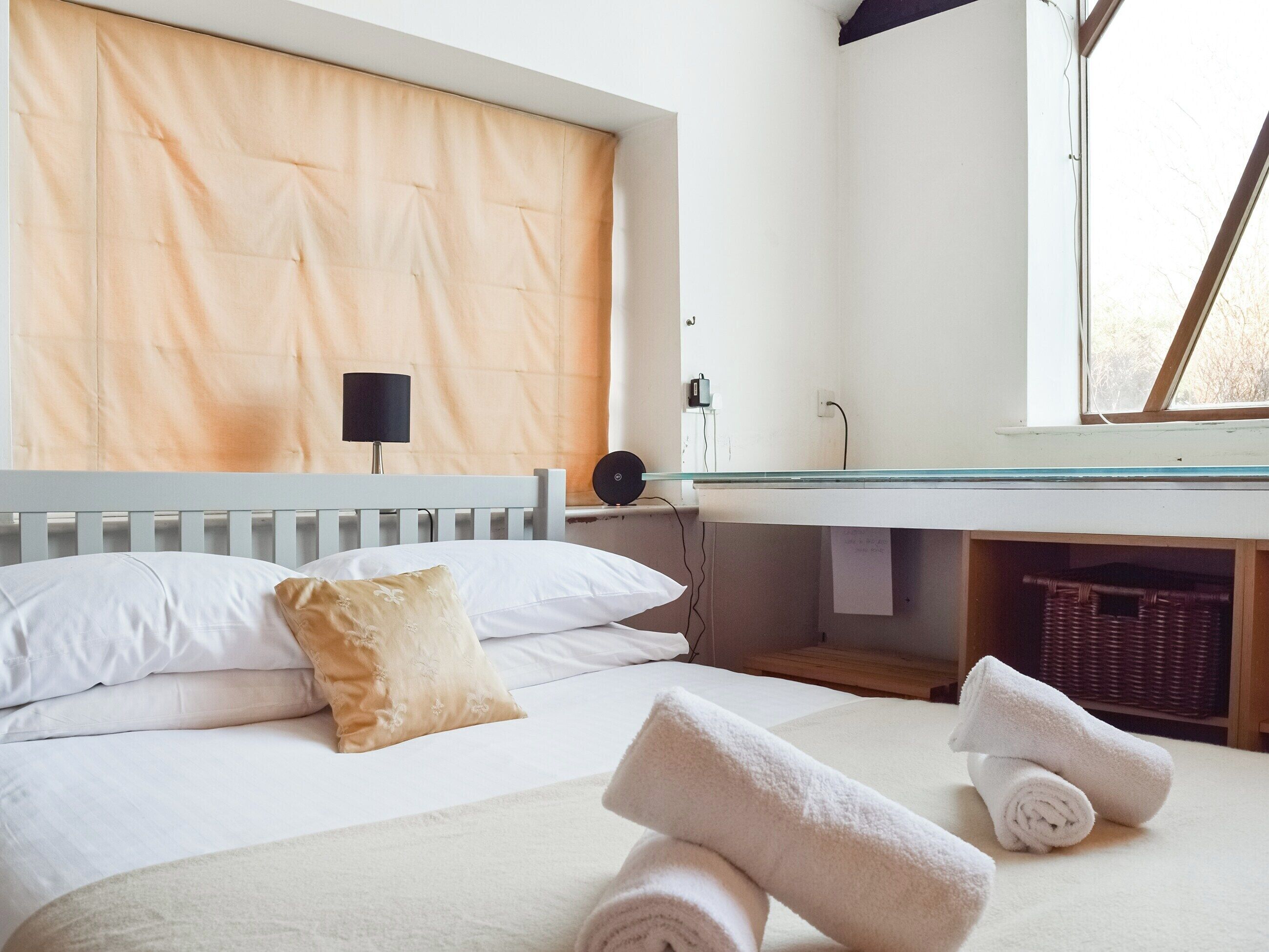 Une chambre à coucher avec un lit, des oreillers, une lampe de chevet, une fenêtre et un miroir.
