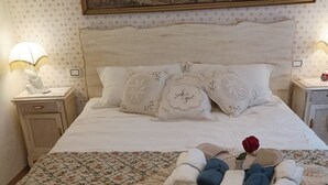 A neatly made bed with floral bedding, a decorative pillow, and a tray of towels. - Stella's House Bed & Breakfast  (Sabbio Chiese)
