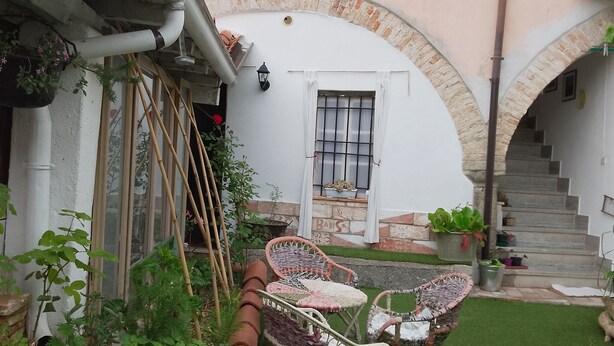 A courtyard with a green lawn, a metal chair, a small table, and a staircase leading to an upper level. - Stella's House Bed & Breakfast  (Sabbio Chiese)