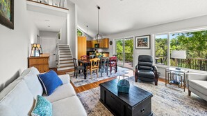 A spacious living area with a sofa, coffee table, and dining table. A staircase leads to an upper level.