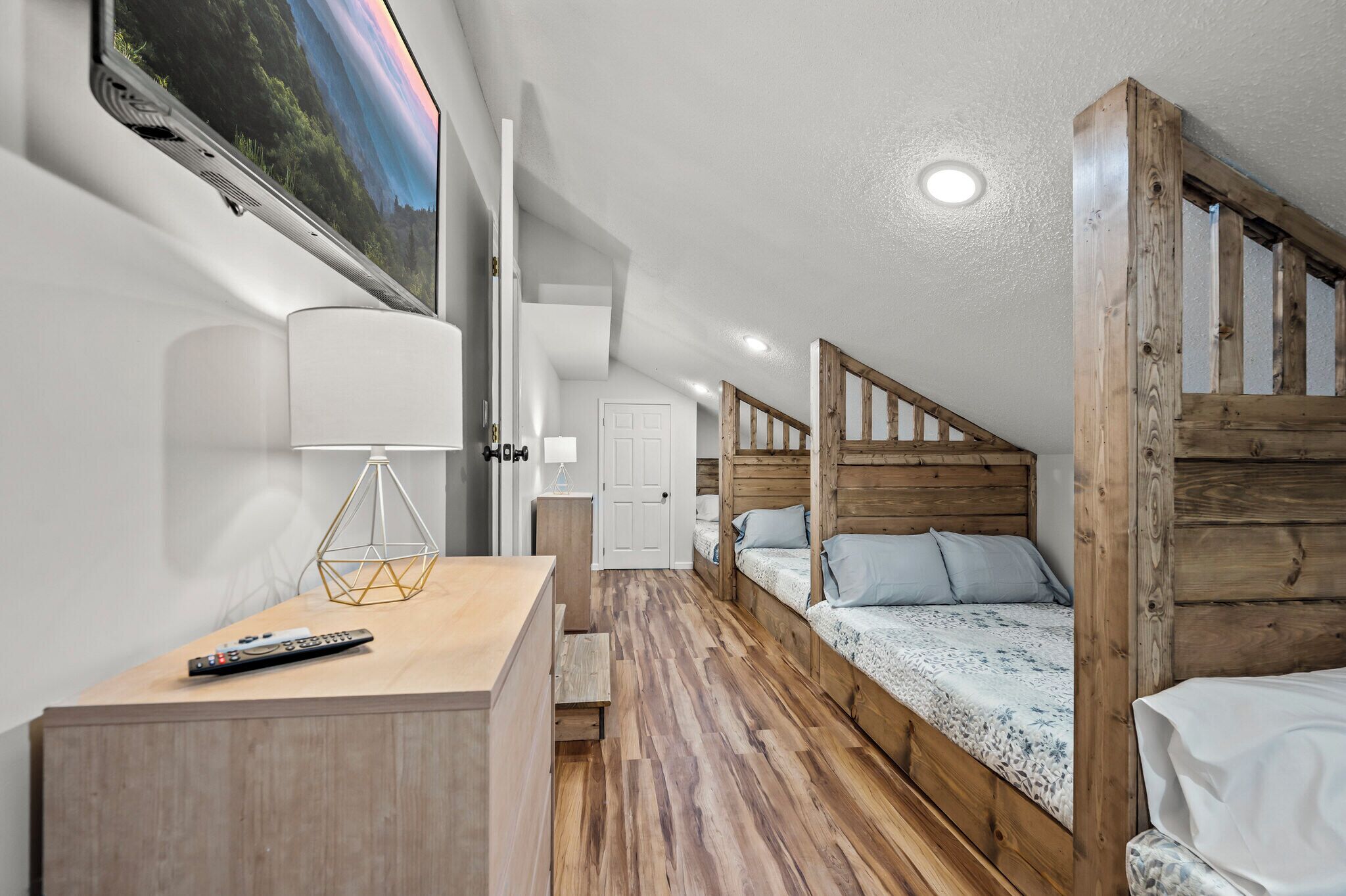 A compact room with a wooden bunk bed, a desk with a lamp, and a TV mounted on the wall.