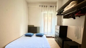 Ein Schlafzimmer mit Bett, Schminktisch, Fernseher und einem Fenster mit Vorhängen.