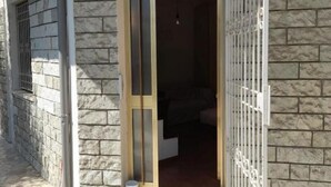 Ein schmaler Flur mit einer Tür zu einem Zimmer, das ein Bett und eine Pendelleuchte beherbergt.
