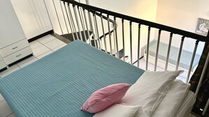 En seng med en turkis madras, hvide puder og en lyserød pude.