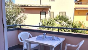 En balkon med et bord og to stole, et lille vindue og en dør.