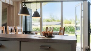 Ett kök med ett stort fönster, en köksbänk med muffins och en modern hänglampa.