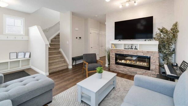 Een moderne woonkamer met een open haard, een flatscreen televisie erboven en een trap die naar een ander niveau leidt.