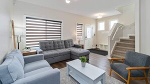 Een moderne woonkamer met een hoekbank, een salontafel en een fauteuil. Er is een trap die naar een ander niveau leidt.