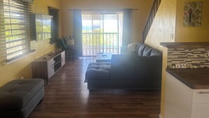A living room with a sofa, a coffee table, and a TV. There is a staircase leading to a balcony. - 2bed 2 bath with Shared Pool and a View. 7 mins to Cruz Bay! 15 mins to Beaches. (St. John)