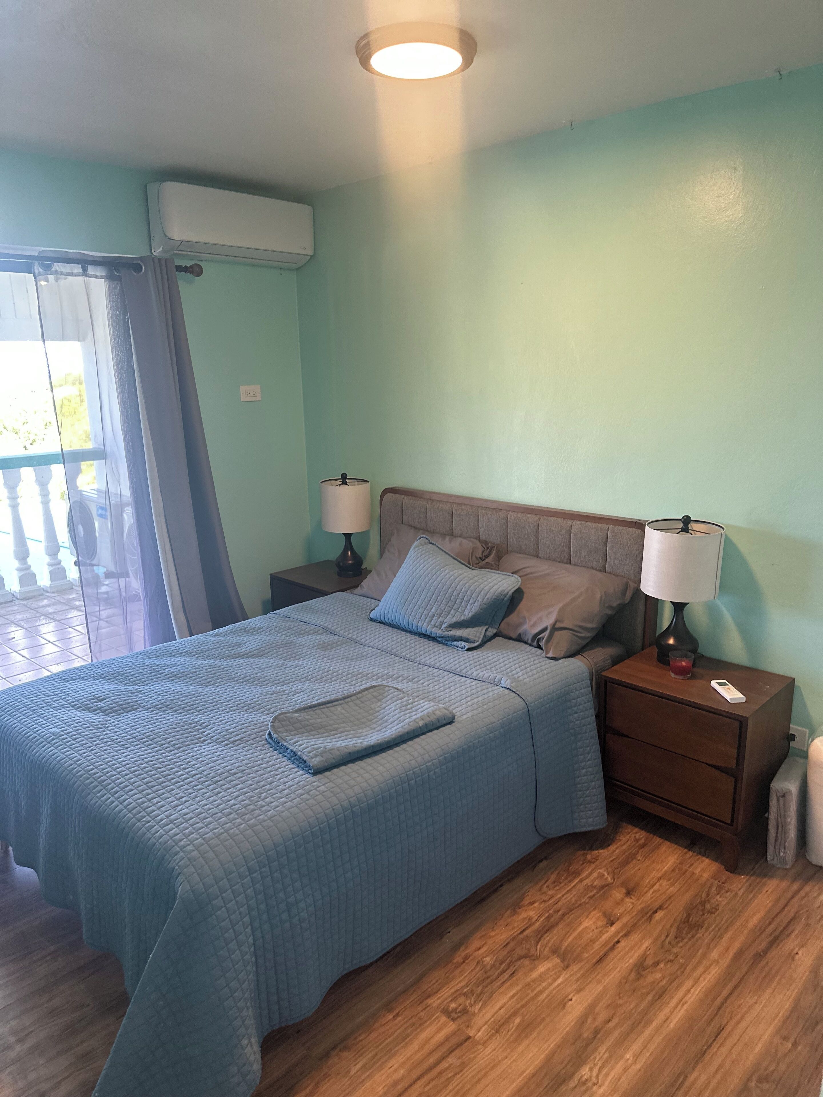 A bedroom with a bed, two bedside tables, a nightstand, a lamp, and a window with a curtain.